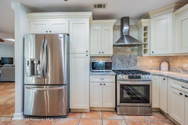 kitchen featuring light stone counters, tasteful backsplash, visible vents, appliances with stainless steel finishes, and wall chimney range hood