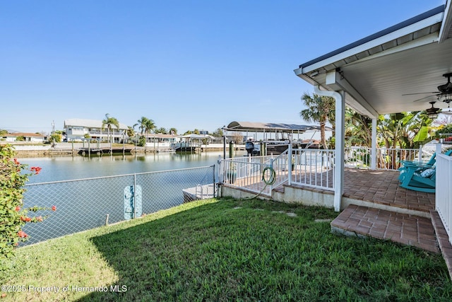 dock area featuring a water view, boat lift, fence, and a lawn