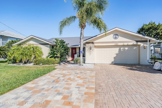 single story home with an attached garage, a front yard, decorative driveway, and stucco siding