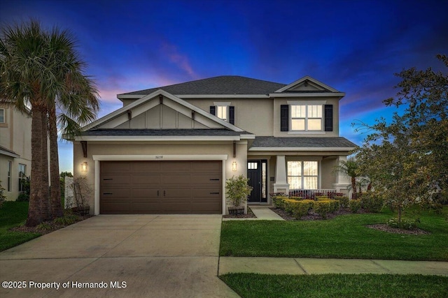 view of front of house with an attached garage, a front yard, roof with shingles, stucco siding, and driveway