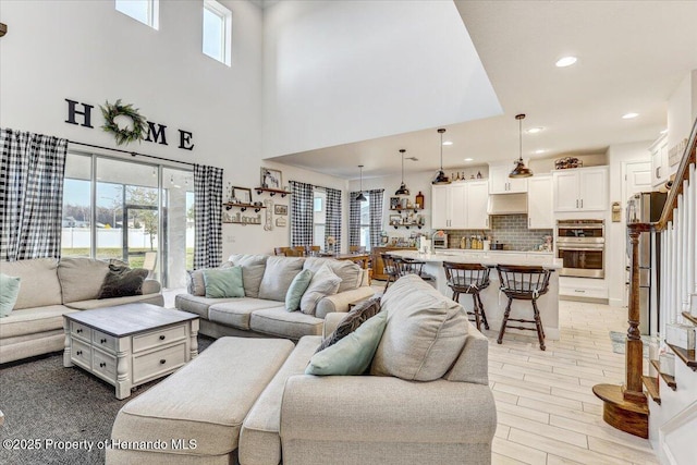 living room with a water view, stairs, recessed lighting, a towering ceiling, and light wood-style floors