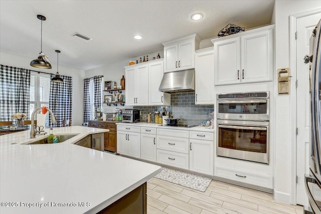 kitchen featuring visible vents, under cabinet range hood, light countertops, stainless steel double oven, and a sink