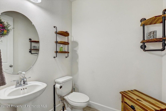 bathroom featuring toilet, baseboards, and a sink