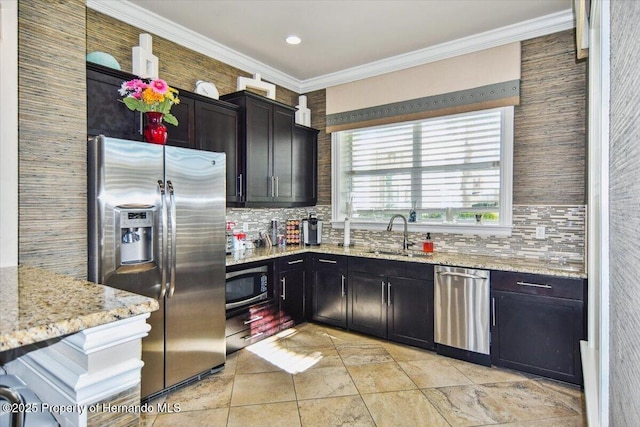 kitchen with a sink, light stone counters, tasteful backsplash, appliances with stainless steel finishes, and crown molding