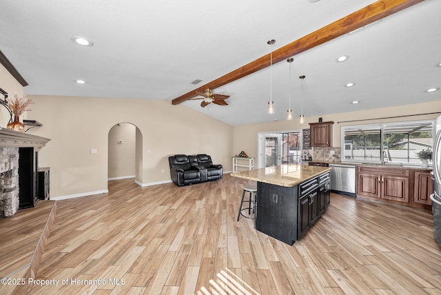 kitchen featuring light stone counters, a breakfast bar area, open floor plan, a center island, and dishwasher