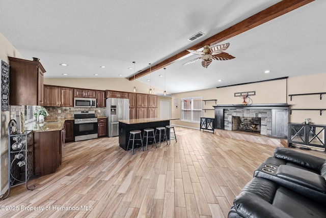 living area featuring vaulted ceiling with beams, a fireplace, visible vents, a ceiling fan, and light wood-type flooring