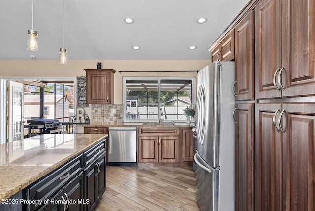 kitchen featuring light stone counters, pendant lighting, stainless steel appliances, backsplash, and a sink