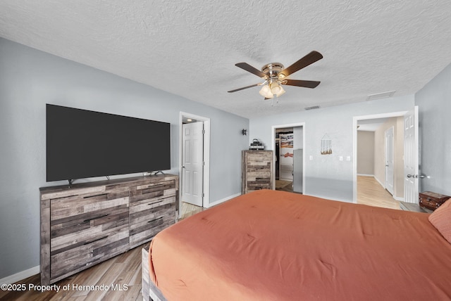 bedroom with visible vents, baseboards, ceiling fan, a textured ceiling, and light wood-style floors