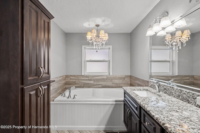 full bath with a chandelier, a textured ceiling, vanity, and a bath