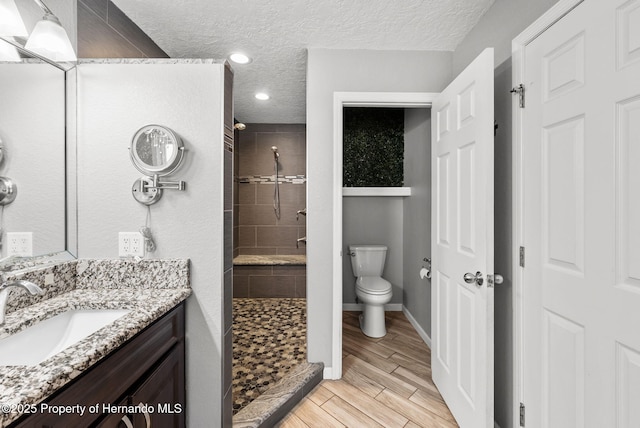 full bathroom with toilet, wood tiled floor, a tile shower, a textured ceiling, and vanity