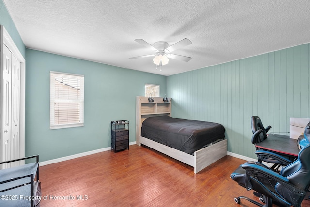 bedroom featuring ceiling fan, multiple windows, wood finished floors, and baseboards