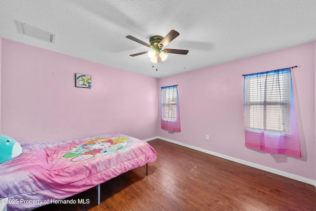 bedroom with visible vents, a textured ceiling, multiple windows, and wood finished floors