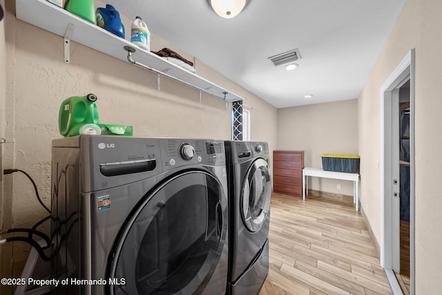 washroom with laundry area, visible vents, baseboards, light wood-style floors, and washer and clothes dryer