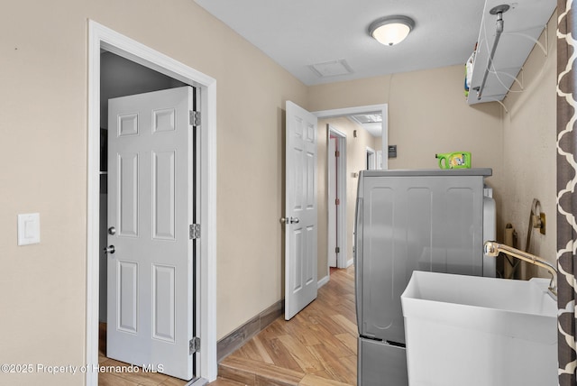 laundry area featuring laundry area, baseboards, washer / clothes dryer, light wood-type flooring, and a sink