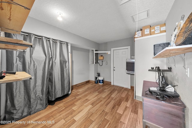 interior space with light wood-style floors, visible vents, a textured ceiling, and baseboards