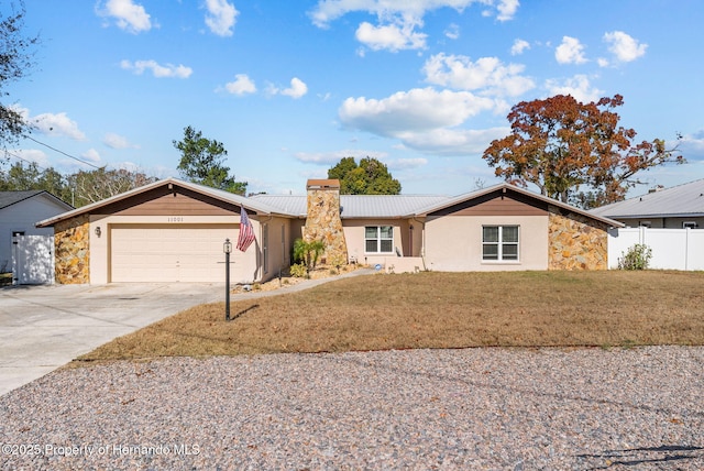 ranch-style house featuring metal roof, a garage, concrete driveway, stone siding, and a front yard