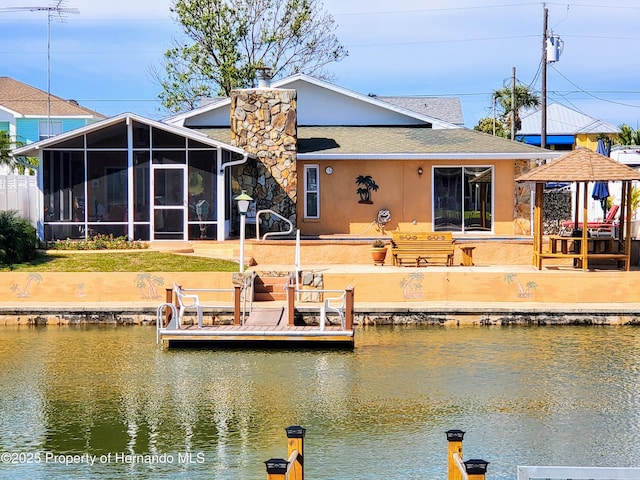 rear view of property with a shingled roof, a sunroom, a water view, and stucco siding