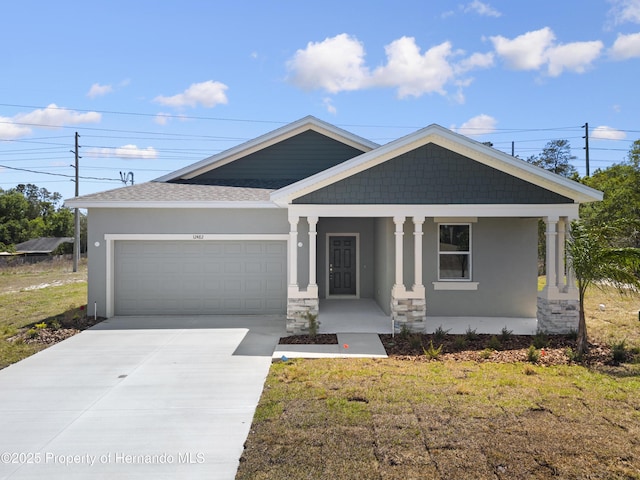 view of front facade featuring roof with shingles, covered porch, stucco siding, a garage, and driveway