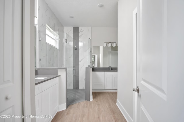 bathroom with two vanities, wood finished floors, a marble finish shower, and a sink