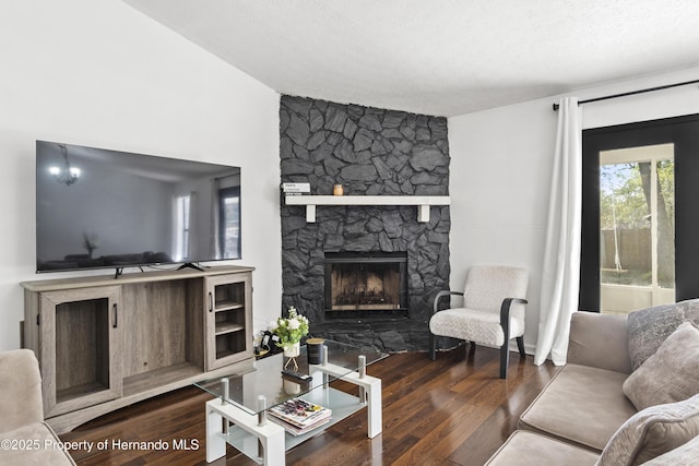 living room featuring vaulted ceiling, dark wood finished floors, a textured ceiling, and a stone fireplace