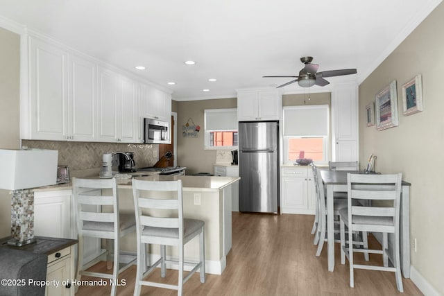 kitchen featuring stainless steel appliances, decorative backsplash, white cabinetry, light wood-type flooring, and a peninsula