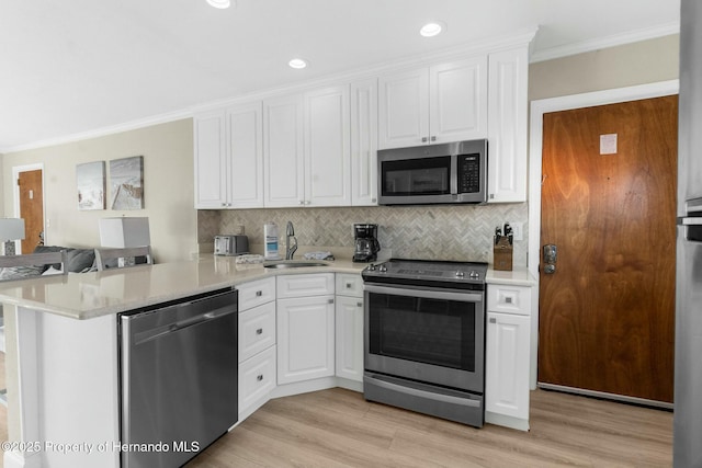 kitchen featuring crown molding, stainless steel appliances, light countertops, white cabinetry, and a peninsula