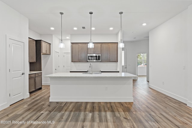 kitchen featuring a sink, stainless steel microwave, a kitchen island with sink, and wood finished floors