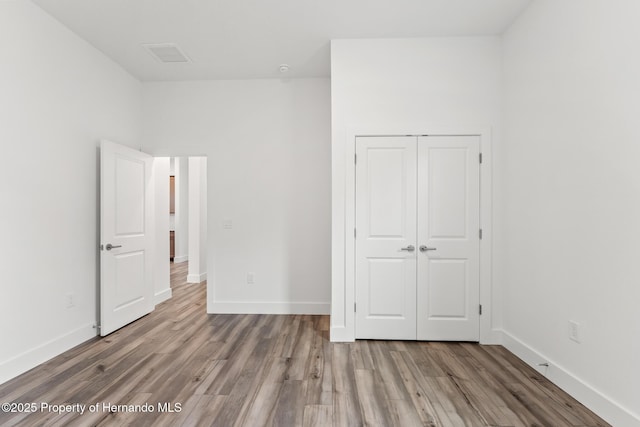 unfurnished bedroom with wood finished floors, baseboards, and a closet