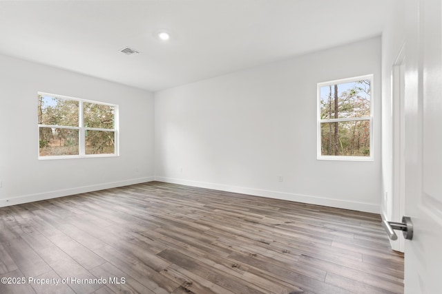 unfurnished room featuring wood finished floors, visible vents, a wealth of natural light, and baseboards