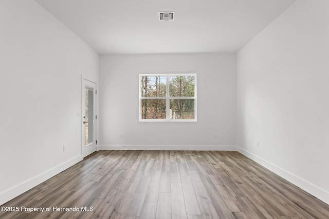 empty room with wood finished floors, visible vents, and baseboards