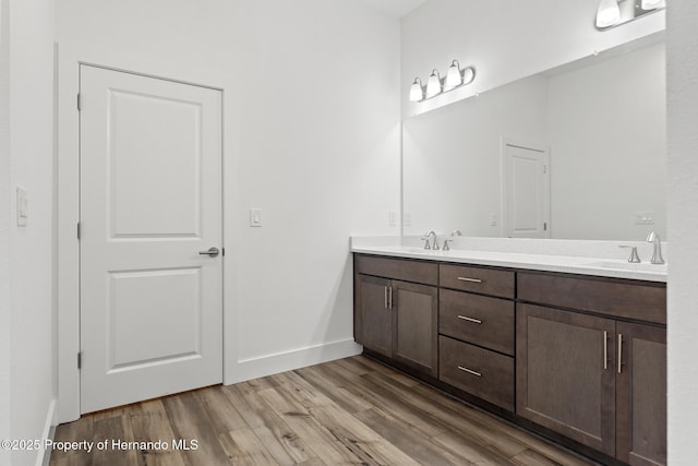 full bath with double vanity, a sink, baseboards, and wood finished floors