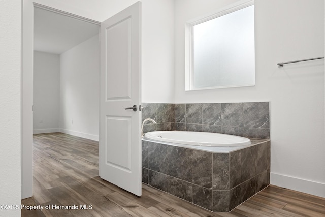 full bathroom featuring baseboards, a garden tub, and wood finished floors