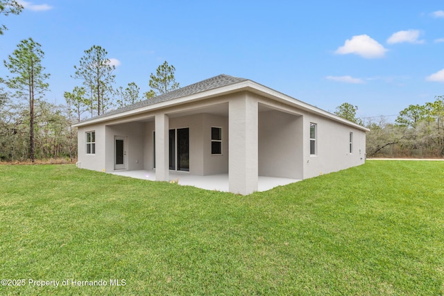 back of house with stucco siding, a patio, and a lawn