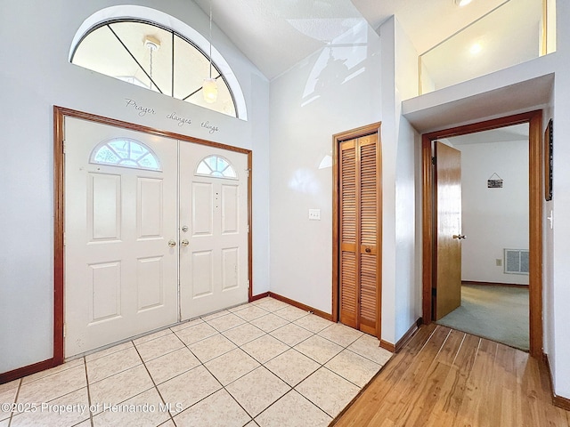 foyer entrance with light wood finished floors, a high ceiling, visible vents, and baseboards