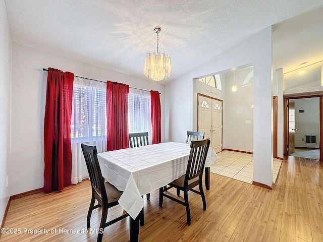 dining space featuring light wood-type flooring, visible vents, vaulted ceiling, and a textured ceiling