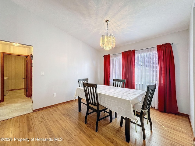 dining room with light wood-type flooring, lofted ceiling, a chandelier, and a textured ceiling