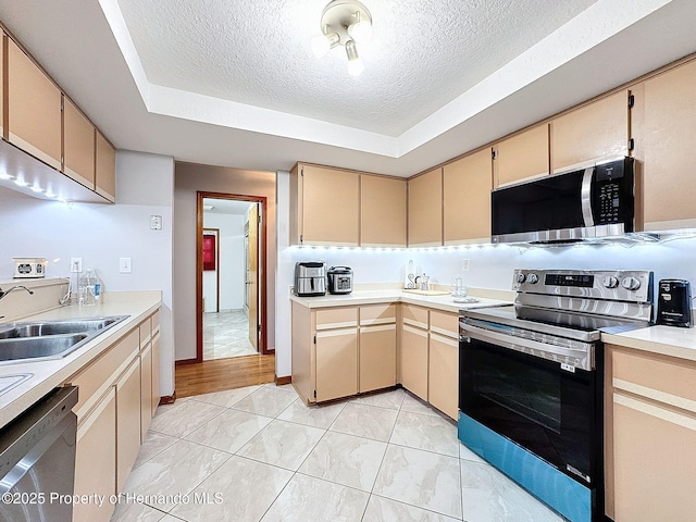 kitchen with a tray ceiling, light countertops, appliances with stainless steel finishes, a sink, and a textured ceiling