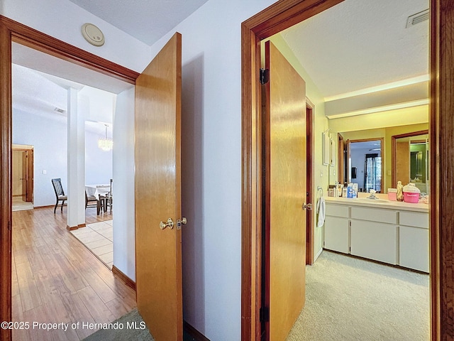 corridor with light wood finished floors, baseboards, visible vents, and a sink