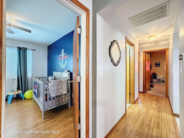 corridor with a textured ceiling, light wood-type flooring, visible vents, and baseboards