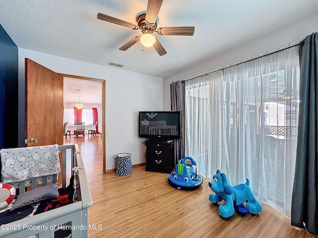 bedroom with a textured ceiling, light wood finished floors, visible vents, and a ceiling fan