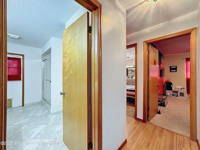 hall featuring light wood-style floors, visible vents, and a textured ceiling