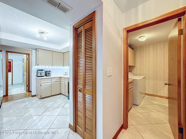 hallway with washer and clothes dryer, light tile patterned floors, visible vents, a textured ceiling, and baseboards