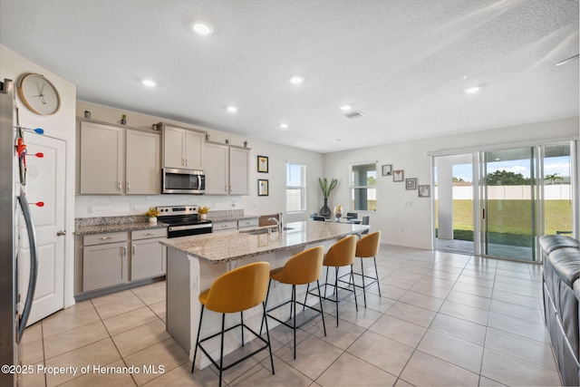 kitchen with light tile patterned floors, appliances with stainless steel finishes, a breakfast bar, gray cabinetry, and a sink