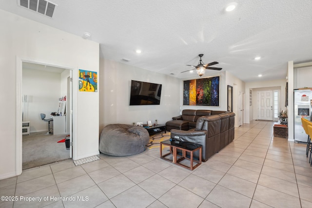 living room featuring a textured ceiling, light tile patterned flooring, visible vents, and a ceiling fan