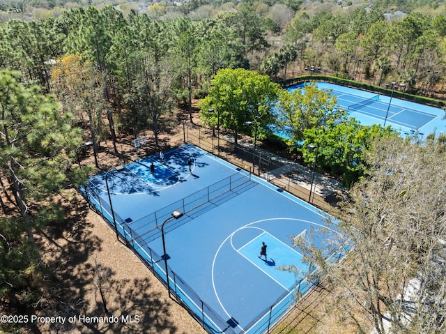 view of sport court featuring a water view, a tennis court, community basketball court, fence, and a forest view