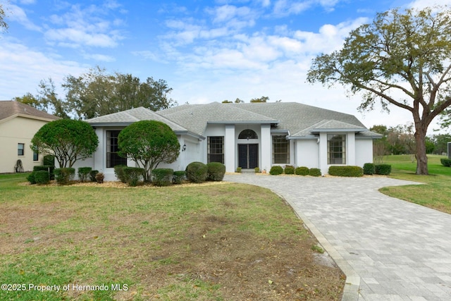 view of front of property with decorative driveway, roof with shingles, a front lawn, and stucco siding