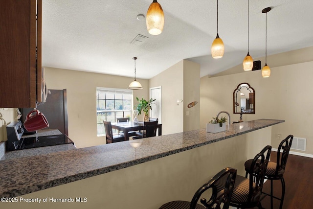 kitchen with visible vents, a kitchen breakfast bar, a textured ceiling, dark wood finished floors, and stainless steel appliances