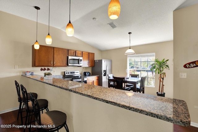 kitchen featuring visible vents, dark wood-type flooring, brown cabinets, a peninsula, and stainless steel appliances