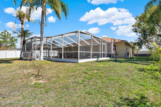 rear view of house with a lanai, a lawn, and fence