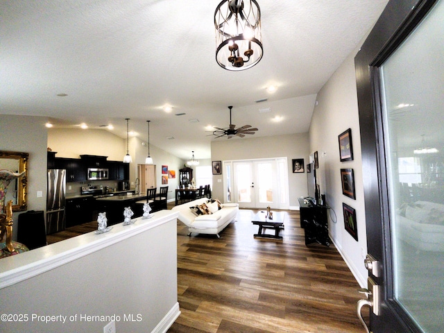 living room featuring vaulted ceiling, dark wood-style flooring, ceiling fan with notable chandelier, and baseboards